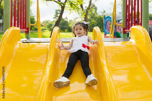 Asian girl happily playing on a playground slide very happy.