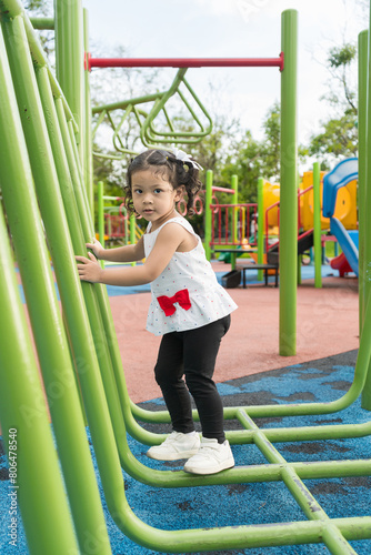 Baby girl balancing on steel beams and cross obstacles in playground .