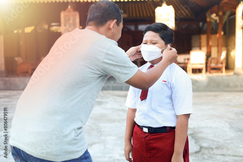 A father puts a mask on an Indonesian student who is going to school