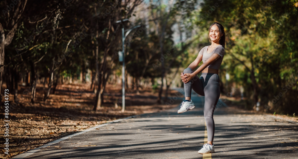 Radiant woman engaged in a standing leg stretch, warming up for her fitness routine on a picturesque forested road. Radiant woman engaged in a standing leg stretch, warming up for her fitness routine on a picturesque forested road.