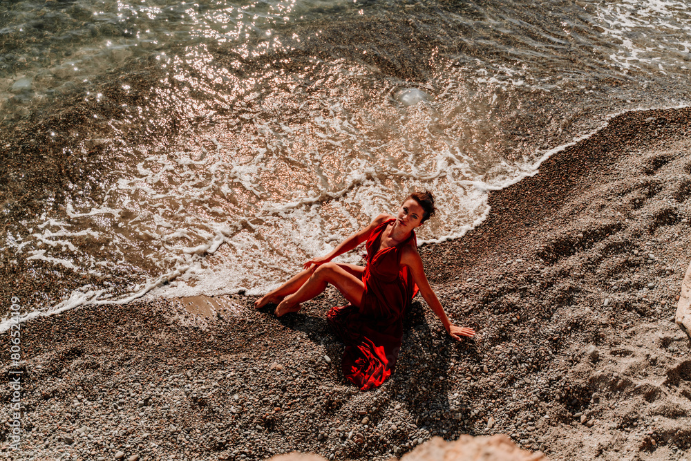 Woman red dress sea. Female dancer in a long red dress posing on a beach with rocks on sunny day Woman red dress sea. Female dancer in a long red dress posing on a beach with rocks on sunny day