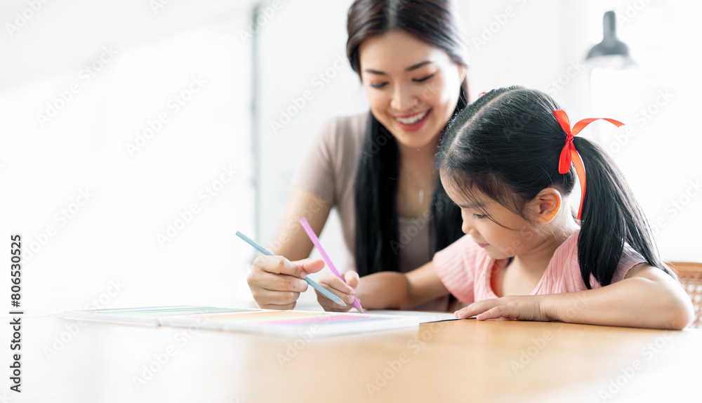 Happy young mother smile with daughter in living room at home, teaching small daughter to reading and writing to develop her daughter skill. Home School Concept Happy young mother smile with daughter in living room at home, teaching small daughter to reading and writing to develop her daughter skill. Home School Concept