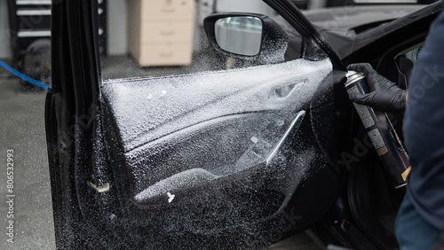 A man sprays cleaning foam on the interior of a car. © Михаил Решетников