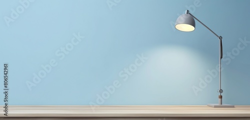 A panoramic view of a minimalist, Scandinavian-style wooden desk with a perfectly aligned, modern desk lamp, captured against a light, ice blue solid background. photo