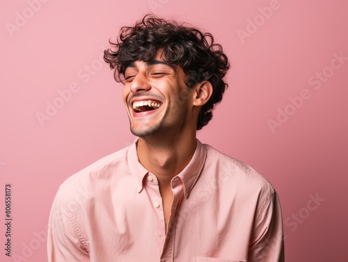 A man with curly hair is smiling and laughing while wearing a pink shirt