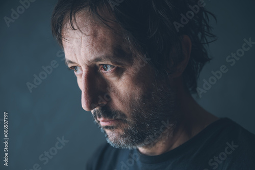 Low key portrait of adult unkempt man in his 40s, looking out the window