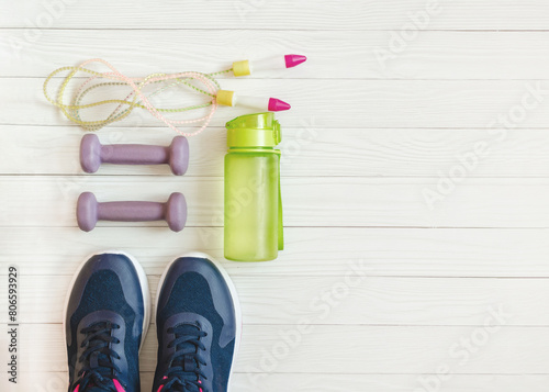 dumbbells, jump rope, water bottle and sports shoes on white wooden background. Fitness background photo