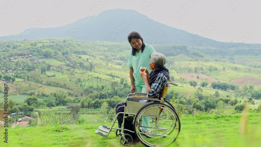 Asian nurse stand beside and hold wheelchair handle with senior man sit on wheelchair also hold a cup of tea and stay near cliff. Asian nurse stand beside and hold wheelchair handle with senior man sit on wheelchair also hold a cup of tea and stay near cliff.