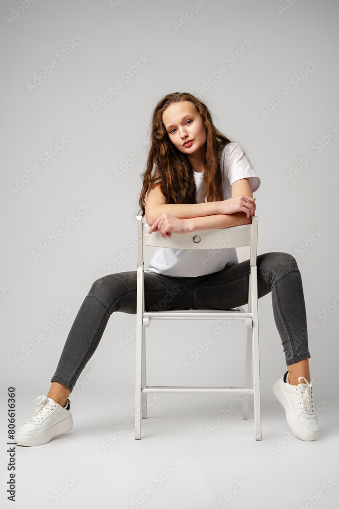 Fototapeta premium Curly girl model posing on a chair against gray background