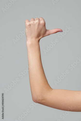 Female hand gesturing thumb up sign on gray background
