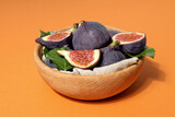 Fresh ripe figs in a wooden bowl on an orange background