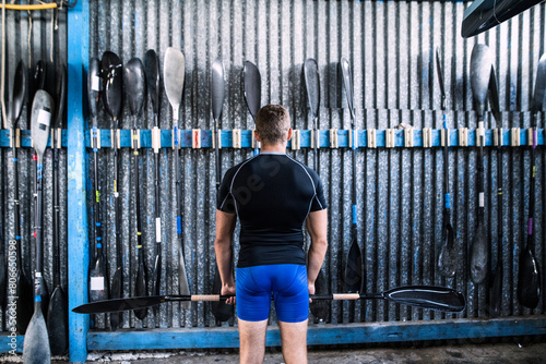 Rear view of young canoeist standing in front of wall with paddles. Concept of canoeing as dynamic and adventurous sport. photo