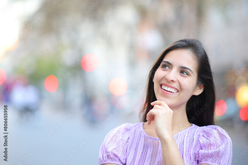 Happy woman thinking looking at side in the street Happy woman thinking looking at side in the street