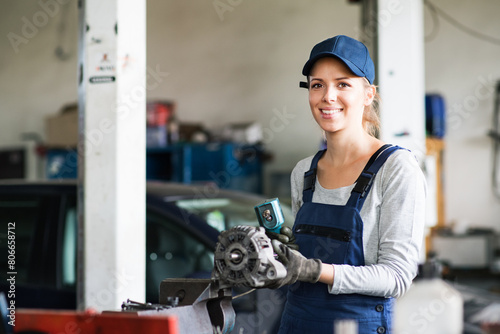 Female auto mechanic repairing, maintaining car. Beautiful woman working in a garage, wearing blue coveralls.