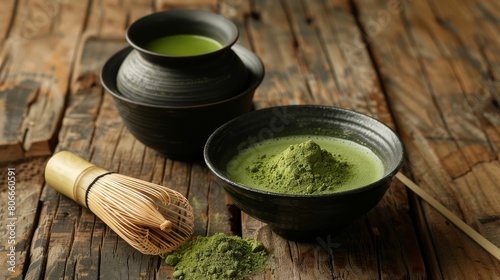 A wooden table with two black bowls. One bowl is filled with matcha powder and the other with matcha tea. A bamboo whisk is sitting on the table next to the bowls.