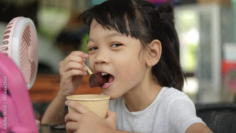 A cute Asian kid girl, aged 8+, was happily eating a small dark brown brownie cake, happily eating her favorite treat. that her mother made on a very special family holiday. A cute Asian kid girl, aged 8+, was happily eating a small dark brown brownie cake, happily eating her favorite treat. that her mother made on a very special family holiday.