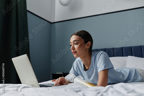 Woman with arm prosthesis using laptop lying on bed in bedroom photo