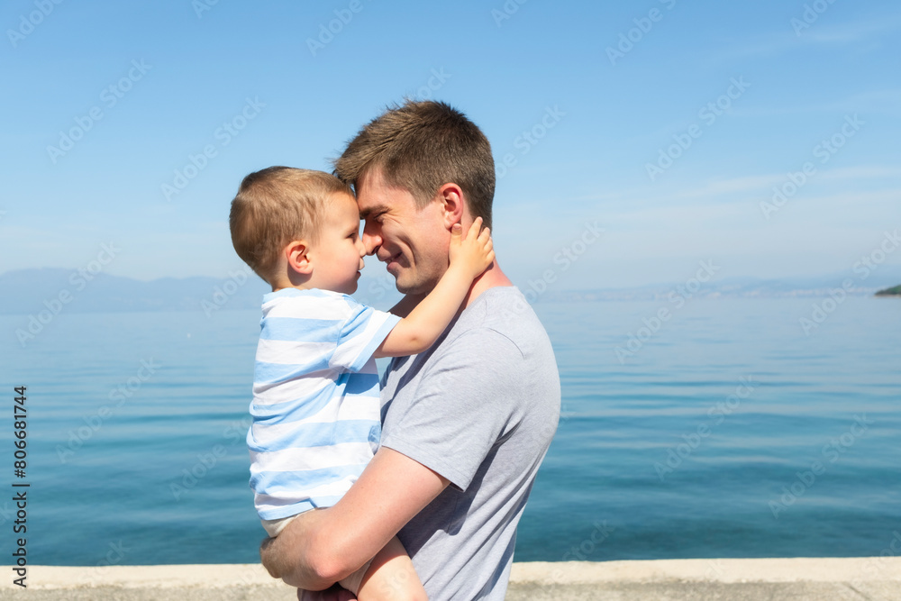 Father embracing son in arms at sea on sunny day Father embracing son in arms at sea on sunny day