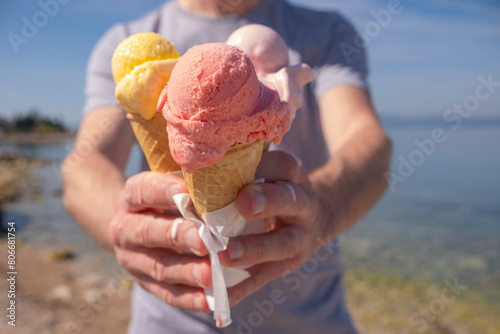 Man holding colorful ice cream in waffle cups on sunny day at seashore