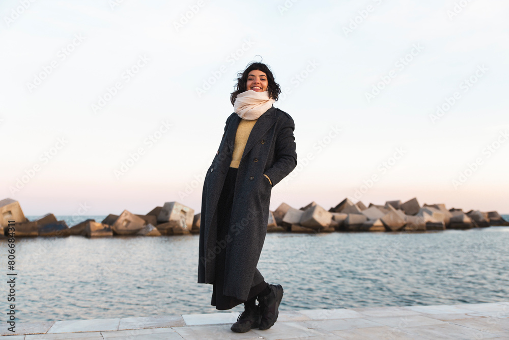 Smiling woman in long coat standing on promenade near sea Smiling woman in long coat standing on promenade near sea