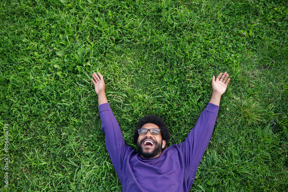 Smiling man with arms outstretched lying on green grass in lawn Smiling man with arms outstretched lying on green grass in lawn
