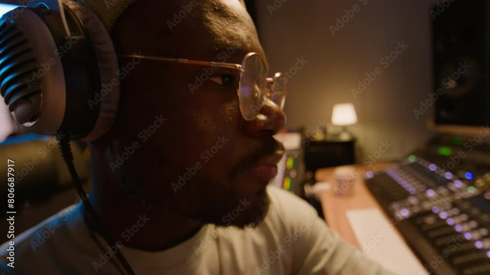 Close-up of face of concentrated African American music producer or DJ sitting in recording studio, listening to music track in headphones, enjoying result and rocking head to rhythm