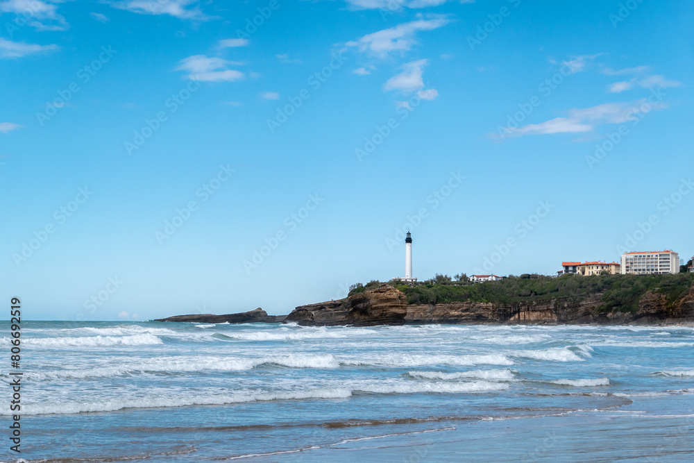 A praia com pequenas ondas, o farol distante em cima de uma grande formação rochosa: A beleza costeira de Biarritz A praia com pequenas ondas, o farol distante em cima de uma grande formação rochosa: A beleza costeira de Biarritz