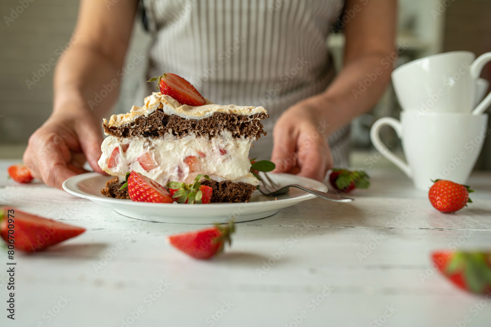 Piece of fresh chocolate strawberry cream cake with meringue topping. Served by a woman with apron 