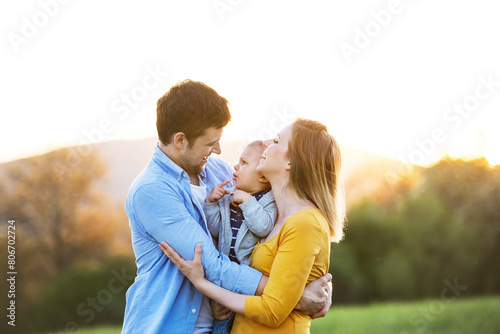 New parents holding small toddler, baby, outdoors in spring nature. Happy family moment