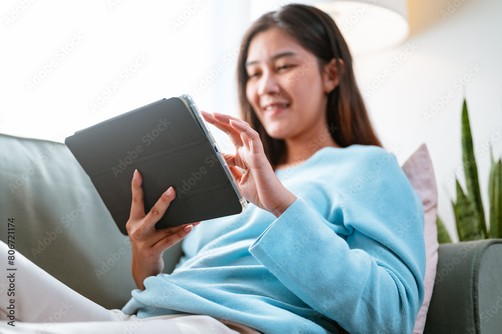 sofa, relax, comfortable, living, women, reading, social, lying, looking, communication. A woman is sitting on a couch and using a tablet. She is smiling and she is enjoying her time. sofa, relax, comfortable, living, women, reading, social, lying, looking, communication. A woman is sitting on a couch and using a tablet. She is smiling and she is enjoying her time.
