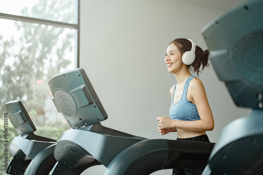 health, fitness, sport, treadmill, muscle, strength, run, runner, trainer, wellness. A woman is running on a treadmill with headphones on. She is smiling and she is enjoying her workout. health, fitness, sport, treadmill, muscle, strength, run, runner, trainer, wellness. A woman is running on a treadmill with headphones on. She is smiling and she is enjoying her workout.