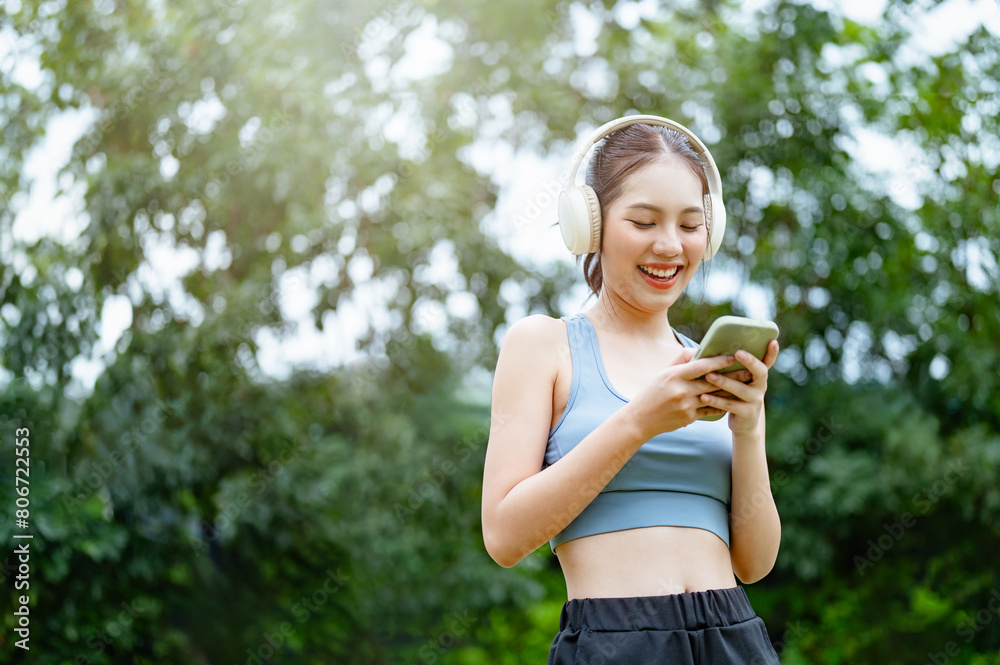 youth, reading, typing, chat, outside, outdoors, happy, smiling, social, message. A woman is smiling and holding a cell phone. She is wearing headphones and she is listening to music. youth, reading, typing, chat, outside, outdoors, happy, smiling, social, message. A woman is smiling and holding a cell phone. She is wearing headphones and she is listening to music.