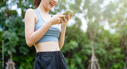 fit  fitness  runner  athlete  smart phone  jogging  person  message  internet  teenager. A woman is smiling and holding a cell phone in her hand. She is wearing a blue tank top and black pants.