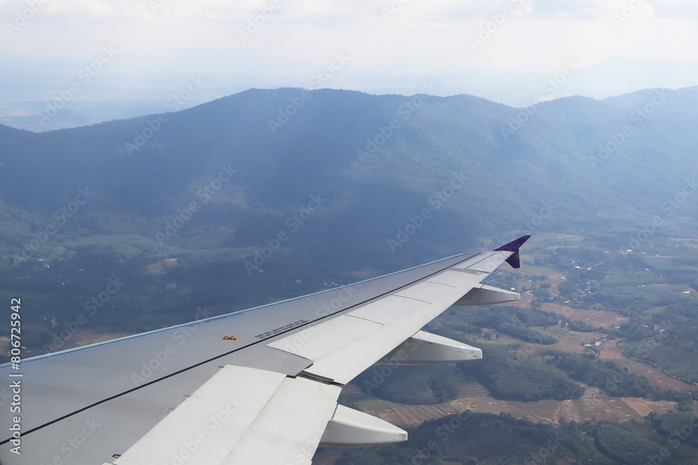 Image view from aircraft window show airplane wing flying with panoramic aerial view of landscape and mountain before landing.