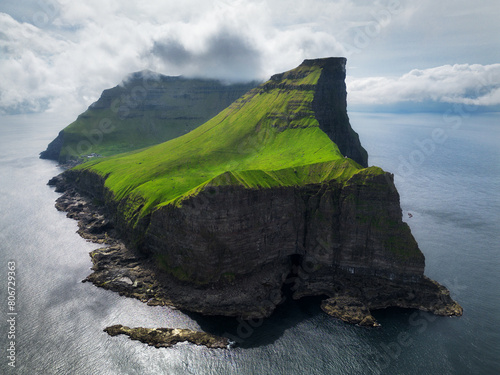 Aerial panorama of a small white lighthouse located on the edge of a huge cliff and the island of Kalsoy. Kalsoy is an isolated small island in the north-east of the Faroe Islands. photo