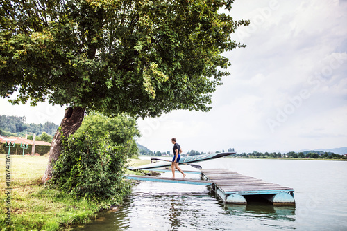 Young canoeist carry canoe and paddle, going into water, walking on wooden dock. Concept of canoeing as dynamic and adventurous sport photo