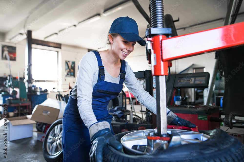 Female auto mechanic changing tieres in auto service, using machinery to removing tire. Beautiful woman working in garage. Female auto mechanic changing tieres in auto service, using machinery to removing tire. Beautiful woman working in garage.