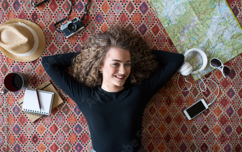 Woman planning summer vacation abroad, going on trip alone. Lying on carpet, daydreaming about adventures.