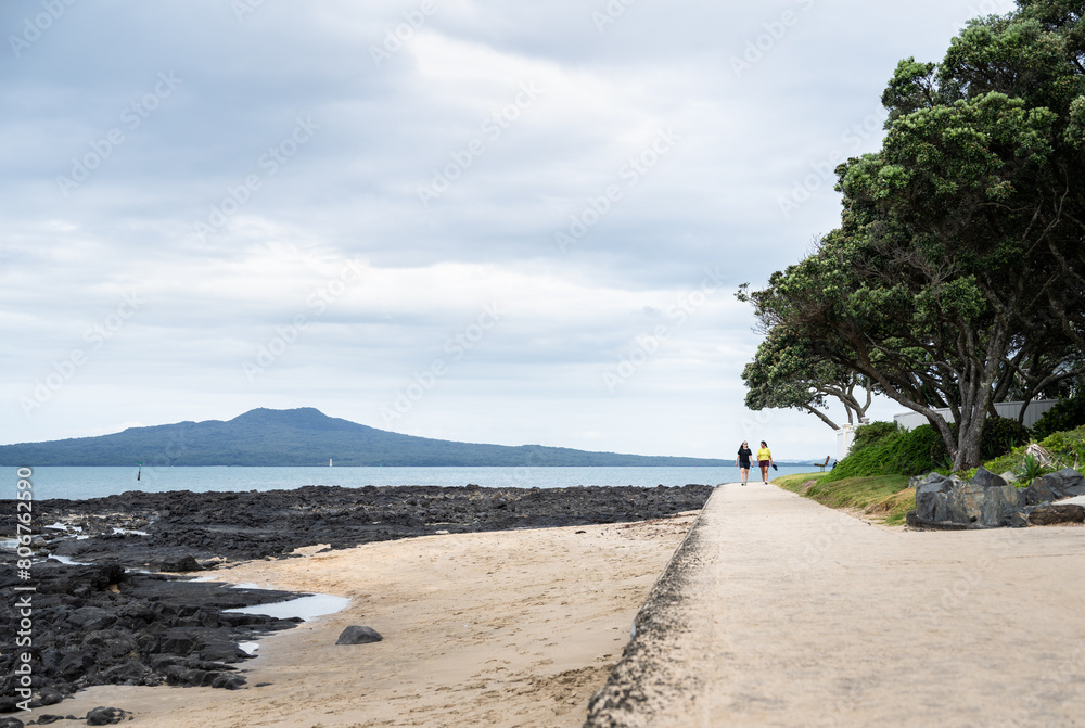 People walking on the beach. Rangitoto Island in the background; Milford Beach. Auckland.
