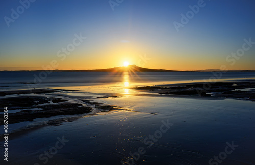 Long exposure image of sunrise over the crest of Rangitoto Island. Milford Beach. Auckland.