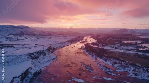   Aerial perspective of a river snaking through a snow-dusted valley, framed by mountaineous backdrop at sunset photo