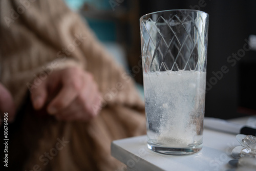 sparkling water glass with dissolving effervescent aspirin pill on table, sick unhealthy man drinking water, taking emergency medicine