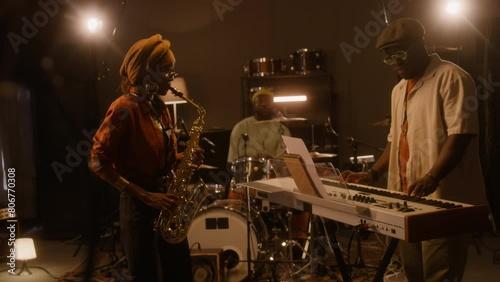 Wallpaper Mural Medium full shot of African American male musician in cap and sunglasses playing keyboards and singing, black woman playing saxophone, bandmate accompanying on drums, while rehearsing in studio Torontodigital.ca