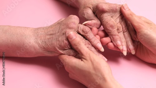 Hands of a young girl stroking the elderly hands with rheumatoid arthritis, on a pink background, supporting a sick person with limited abilities