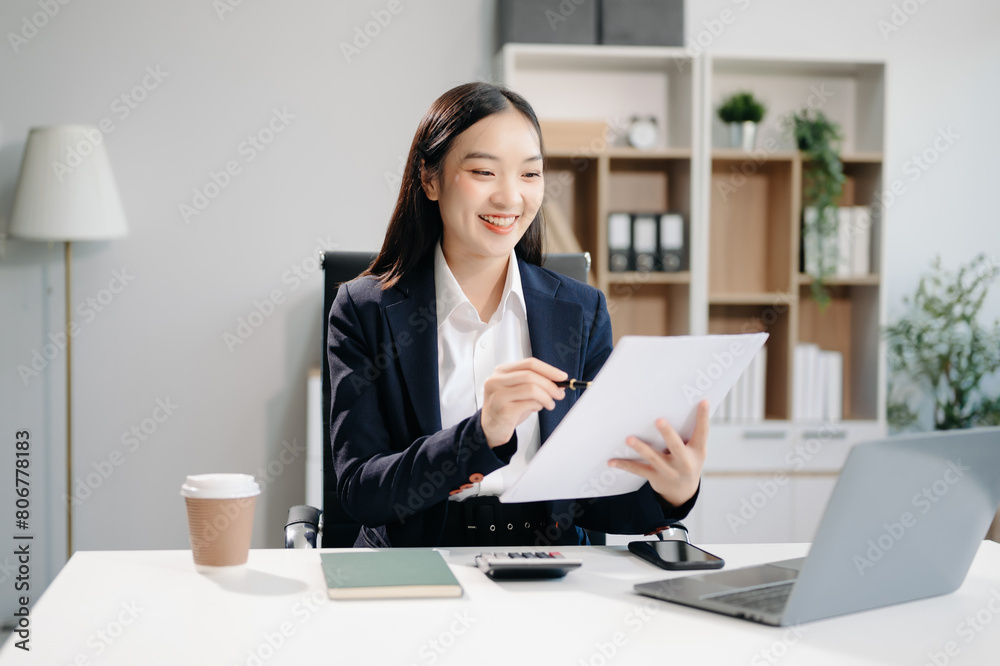 Asian woman using laptop and tablet while sitting at her working place. Concentrated at work. Asian woman using laptop and tablet while sitting at her working place. Concentrated at work.