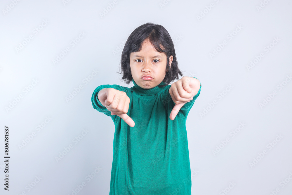 Disappointed Asian little girl gesturing thumbs down over grey background Disappointed Asian little girl gesturing thumbs down over grey background