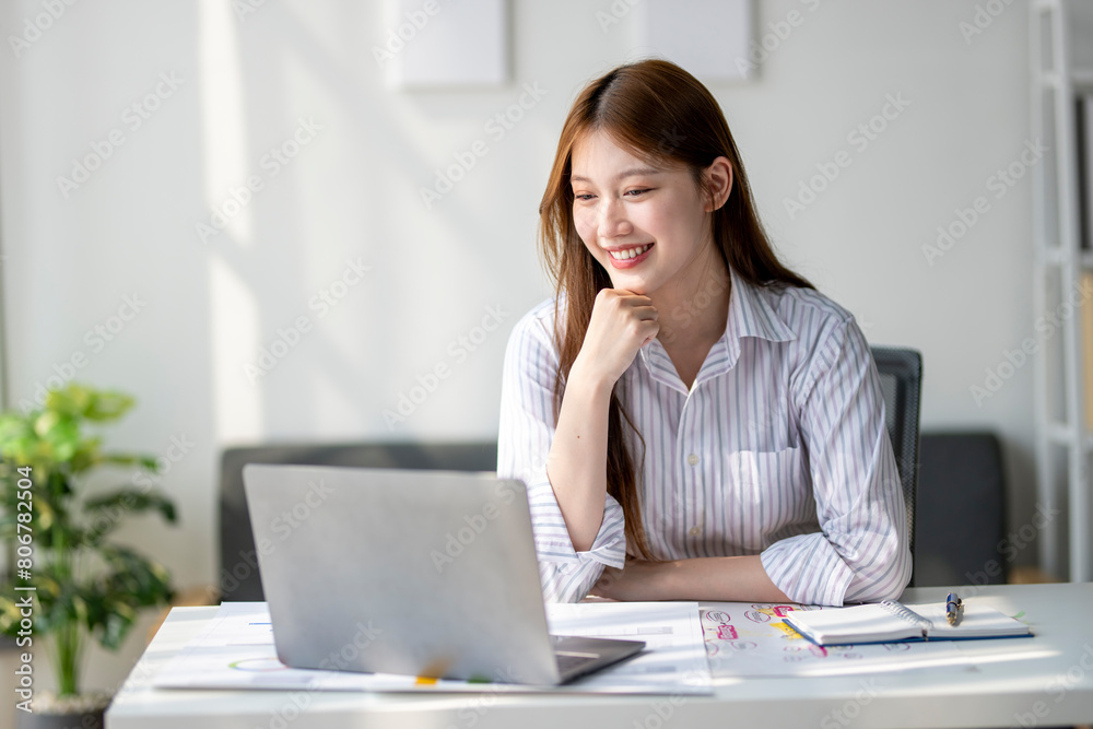 A woman is sitting at a desk with a laptop in front of her. She is smiling and she is enjoying her work A woman is sitting at a desk with a laptop in front of her. She is smiling and she is enjoying her work