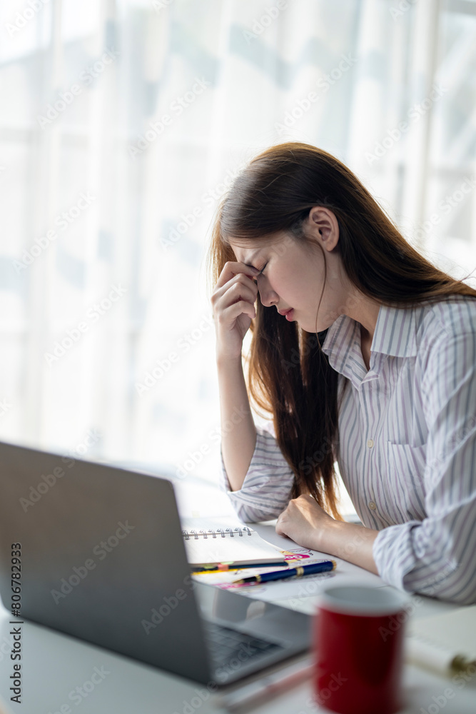 A woman is sitting at a desk with a laptop and a notebook. She is looking at the laptop and she is in a state of distress A woman is sitting at a desk with a laptop and a notebook. She is looking at the laptop and she is in a state of distress