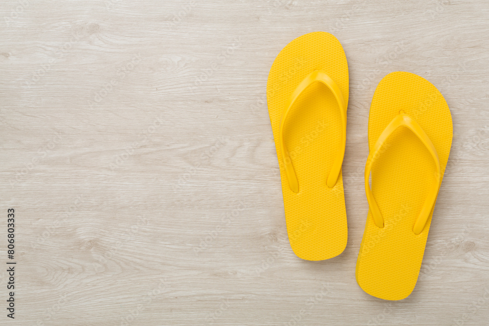 Bright yellow flip-flops on wooden background, top view. Summer concept