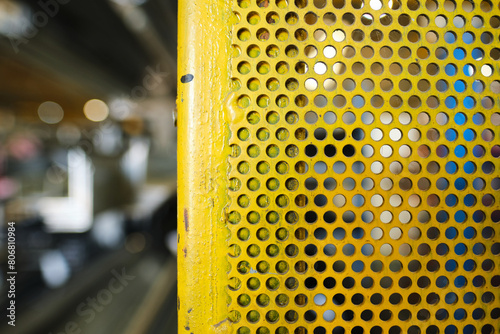 A Galvanised perforated metal sheet painted yellow. industrial machinery metal texture background, showing signs of scratches, usage. Beautiful industrial arty textured background